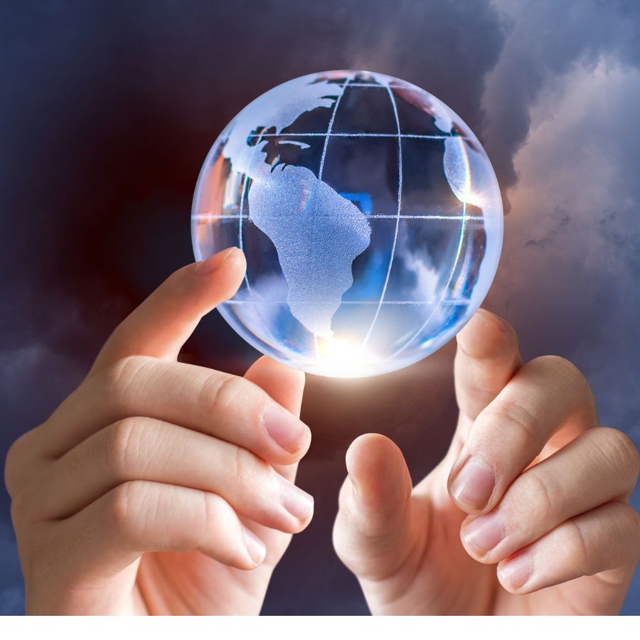 Two hands hold a transparent glass globe with a map of the world, against a cloudy, dark background.